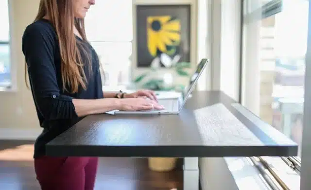 Female student typing on laptop at compact standing desks for students setup near bright window