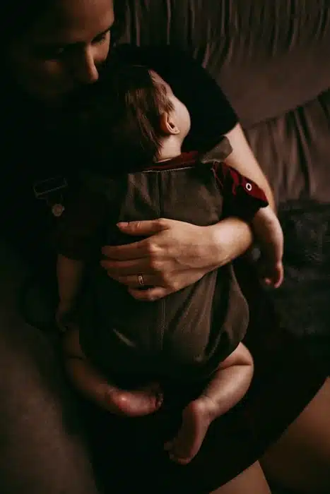 Mom holding her baby close while using a sustainable babywear carrier on the couch