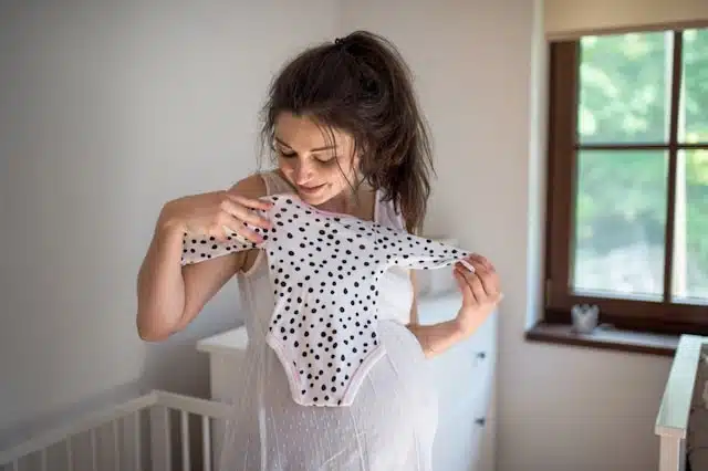 Expecting mom holding up an organic cotton onesie in the nursery