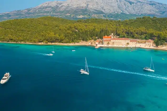 aerial view of Badija Island with sailboats on turquoise waters and a stone monastery along the Dalmatian Coast