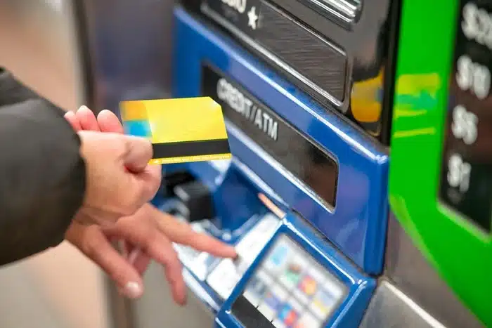 A hand inserting a gold credit card into a blue ATM machine, highlighting the risk of card skimming for travelers.