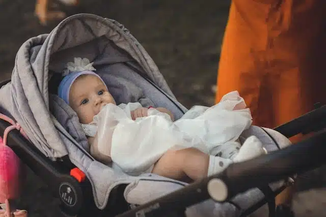 Baby dressed in white sitting in a stroller outdoors