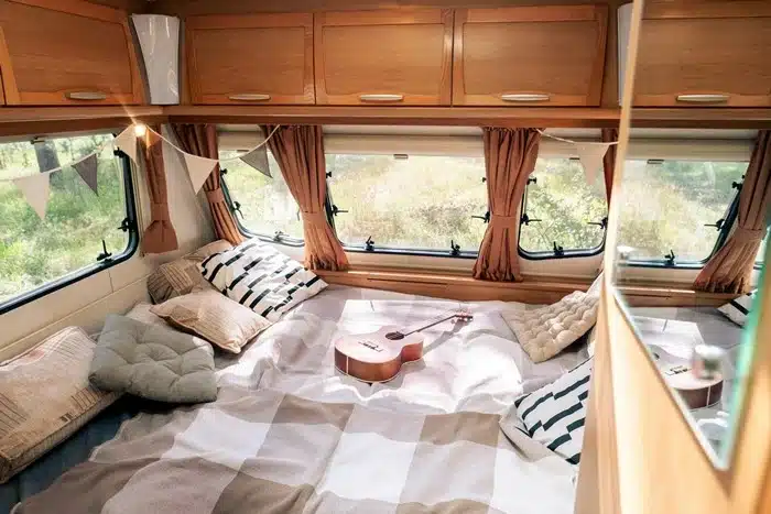 comfortable bed inside a motorhome with a guitar, soft pillows, bunting décor, and large windows with nature views