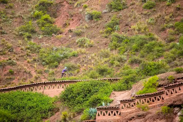 Solo cyclist on a hillside trail overlooking Urubamba's stepped terraces