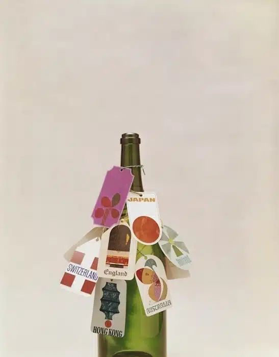 A wine bottle decorated with travel tags from countries including Japan, Switzerland, England, Australia, and Hong Kong — how to bring wine from holiday as a souvenir