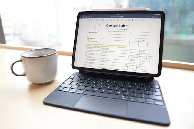 A tablet displaying an opening budget spreadsheet on a desk next to a coffee mug