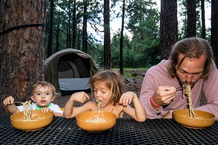 Dad and two children enjoying a pasta meal outdoors at a forest campsite
