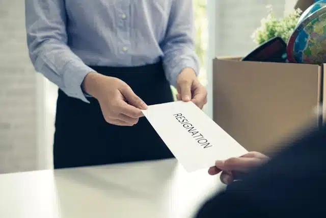 A person submitting a resignation letter across a white desk as part of a career switch