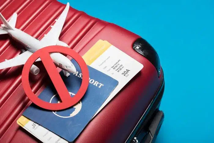 A red suitcase with a passport, boarding pass, and a prohibition sign representing common scams targeting travelers to watch out for.