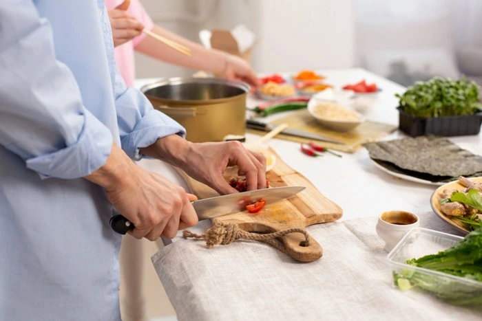 Two people in a culinary travel tips cooking class, chopping fresh chilli on a wooden board surrounded by local ingredients