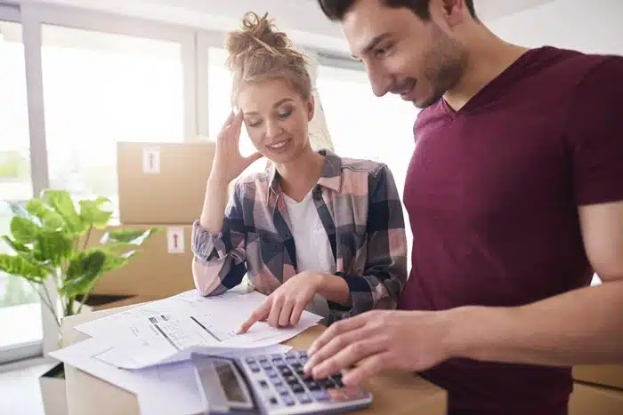 Couple reviewing moving costs and budget paperwork with a calculator near packed boxes