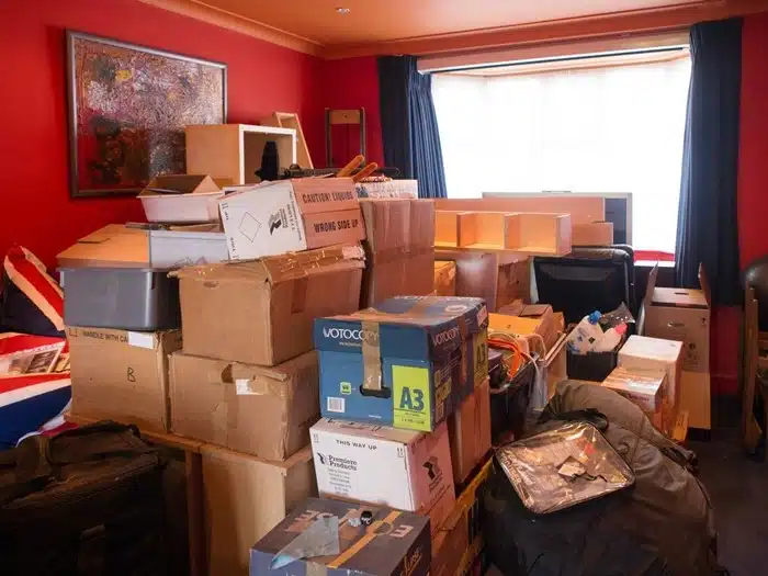 Stacked moving boxes and packed belongings in a red-walled living room before relocation to NYC