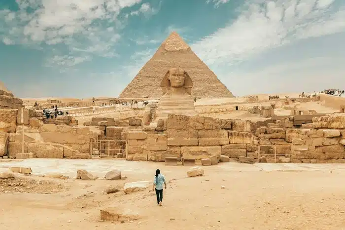 Person walking across the sandy Giza plateau toward the Great Sphinx and pyramid in Egypt