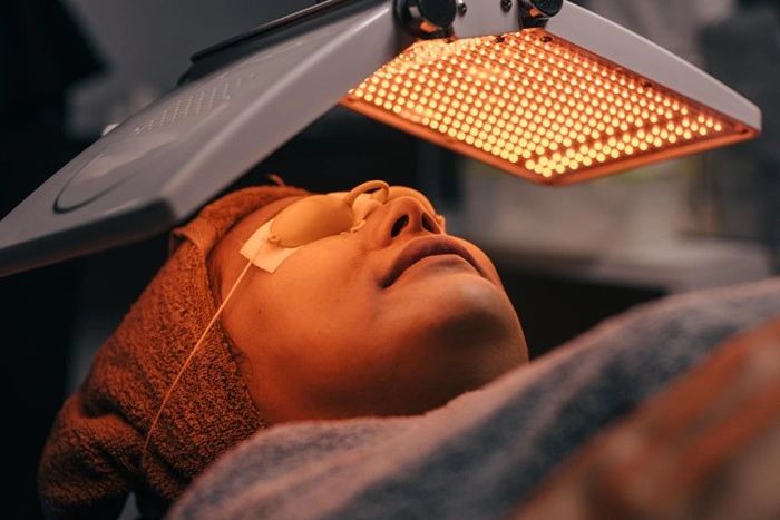 A woman receiving a pico laser for skin rejuvenation treatment under a professional LED laser panel at an aesthetic clinic