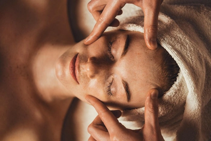Esthetician performing a professional facial treatment on a woman with visible dark spots and uneven skin tone