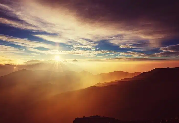 Sunrise over Haleakalā volcano summit in Maui with golden light spreading across layered mountain silhouettes
