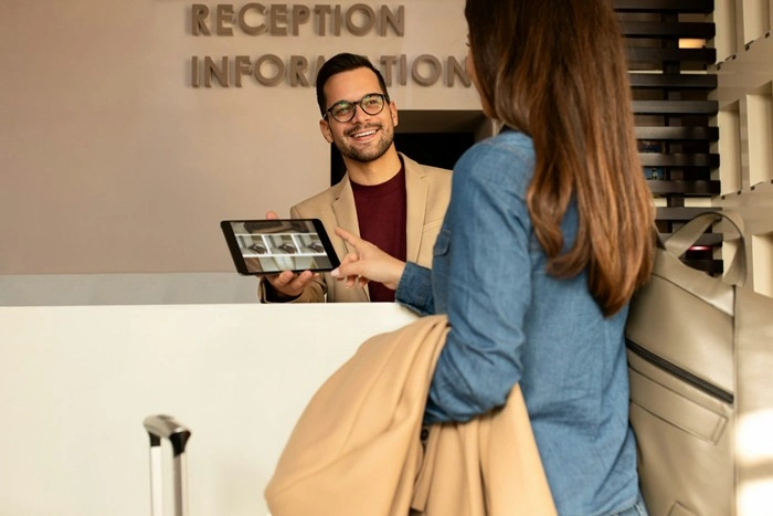 Hotel receptionist showing accommodation options on a tablet to a guest at check-in