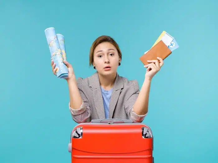 A concerned female traveler holding a globe map and airline tickets next to a red luggage bag, emphasizing the need to stay alert against travel fraud.