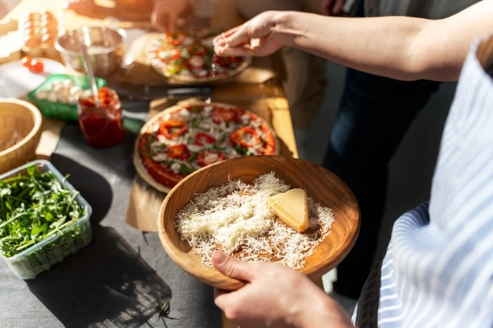 Hands assembling fresh pizza with grated cheese and toppings during a culinary cooking class in Italy