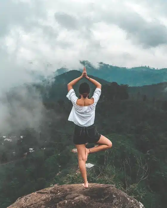 A life transformation journey captured through a woman holding a yoga pose on a rocky cliff overlooking misty mountains