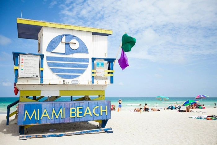 Colorful Miami Beach lifeguard stand with turquoise ocean and beachgoers — travel essentials for Miami on a budget