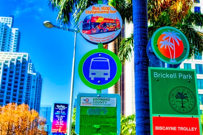 Miami Brickell Park bus stop signage with Broward County express and city sightseeing tour signs against a blue sky