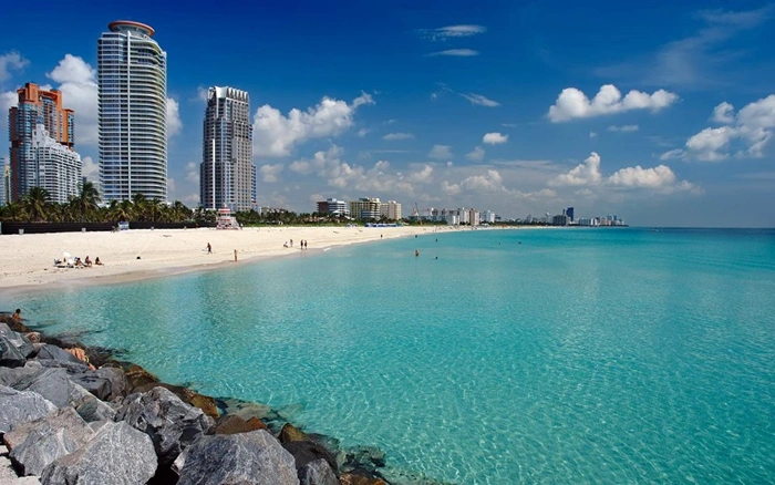 Turquoise waters and white sand beach at South Pointe Miami with luxury high-rise buildings along the shoreline