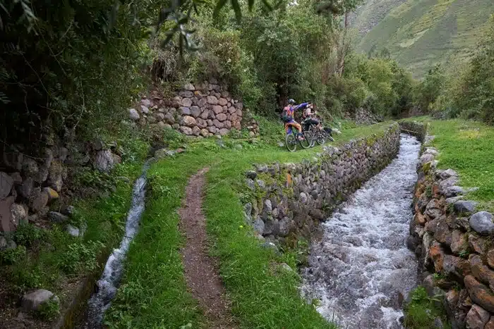 Mountain bikers riding alongside a stone-lined irrigation canal in the Sacred Valley
