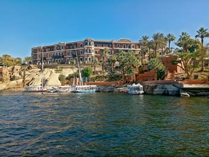 Feluccas and boats moored along the Nile River in Aswan Egypt with a grand hotel and palm trees in the background