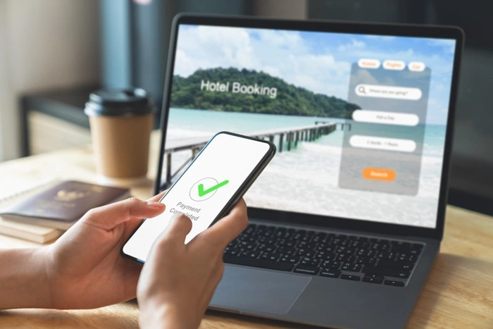 Person completing an online hotel booking on a laptop with a payment confirmed notification on their smartphone