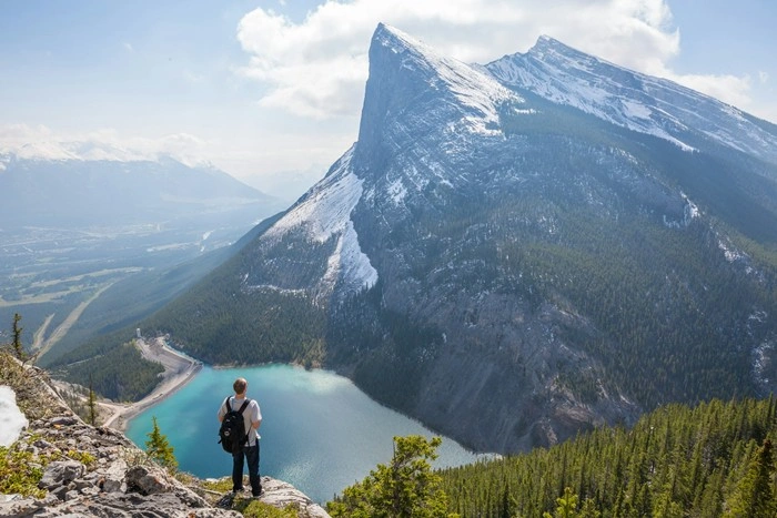 Hiker standing on a mountain summit overlooking a turquoise lake and snow-capped peaks — how to redefine lifestyle through outdoor living and adventure