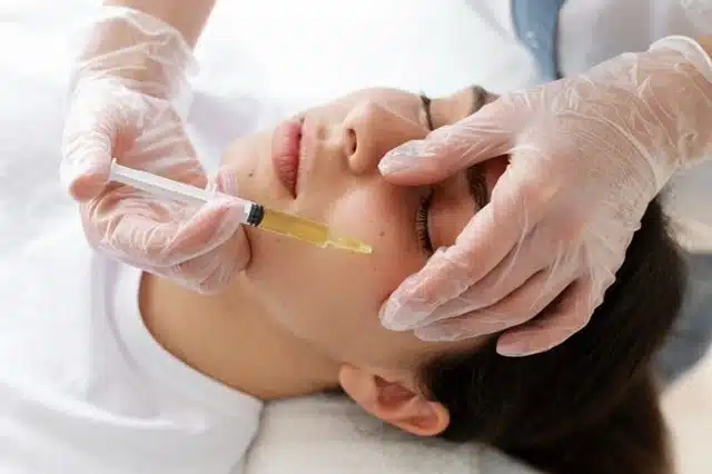 A woman receiving a peptide benefits for travelers facial treatment with a syringe administered by a gloved medical professional