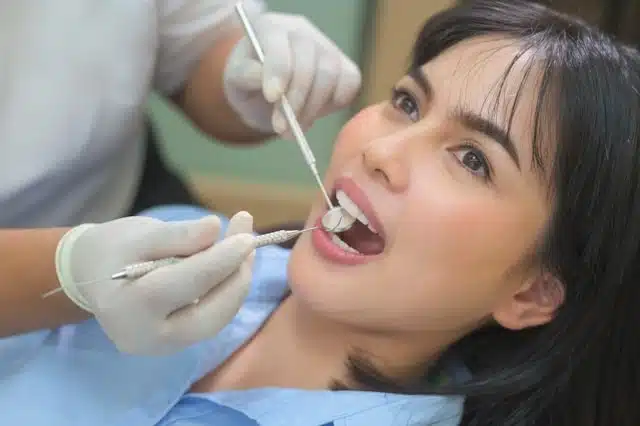 Woman receiving a dental examination from a dentist using clinical tools before traveling Singapore