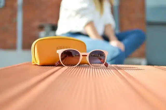 Pink sunglasses with a yellow case resting on a wooden table outdoors