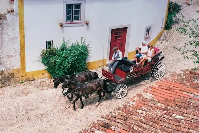 Tourists on a private horse-drawn carriage tour through the cobblestone streets of Óbidos, Portugal
