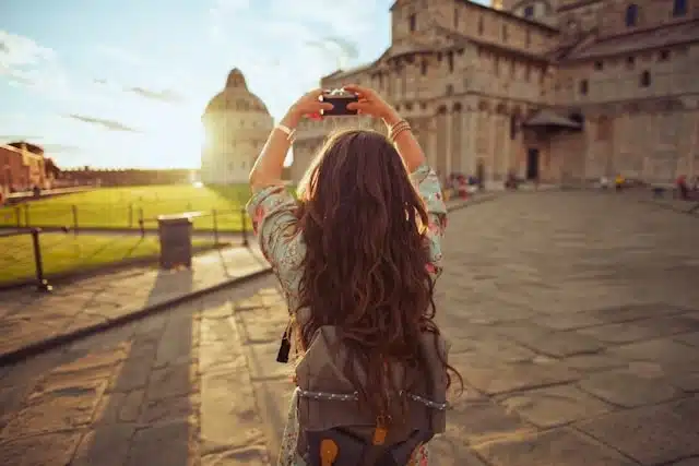 A solo female traveler photographing the Piazza dei Miracoli and the Leaning Tower of Pisa at golden hour in Italy