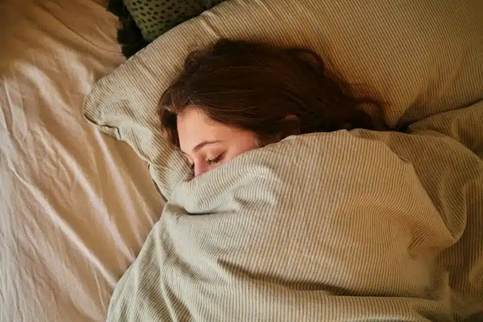Woman sleeping peacefully under a cozy blanket, prioritizing rest and self care during stressful change