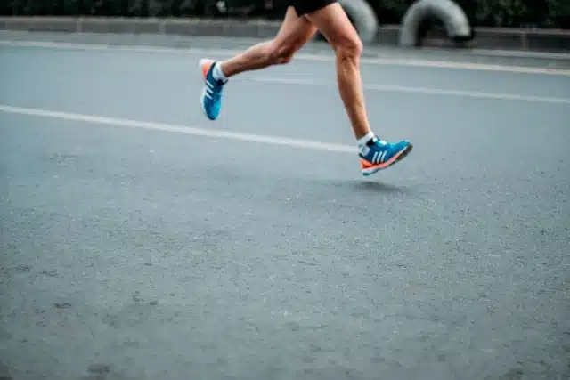 A person running on an asphalt road wearing blue and orange sneakers to maintain fitness