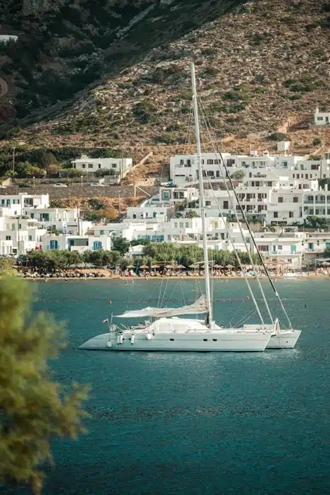 A sailing trip in Greece with a white catamaran anchored off the coast of Sifnos, with a hillside village of whitewashed buildings in the background