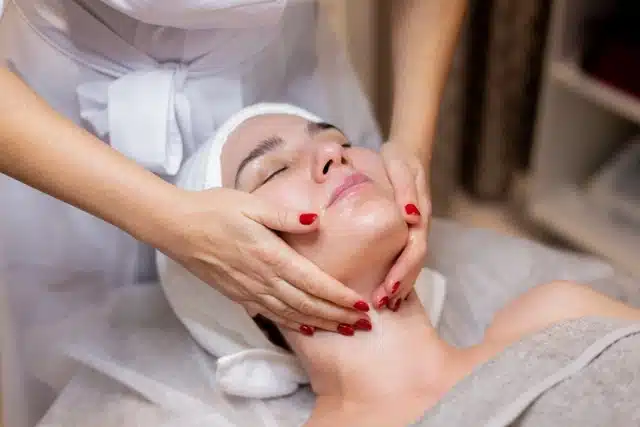 A woman receiving a facial skin treatment from a therapist to restore skin health benefits after traveling