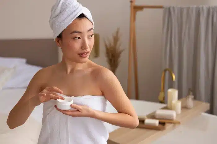 a woman in a towel applying moisturizer as part of her skincare routine while traveling
