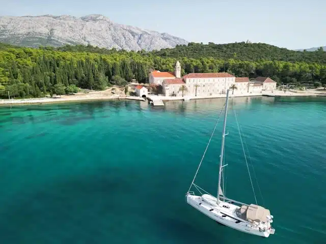 slow travel with a yacht on the turquoise waters of the Adriatic coast, with a historic Croatian monastery and forested hillside in the background