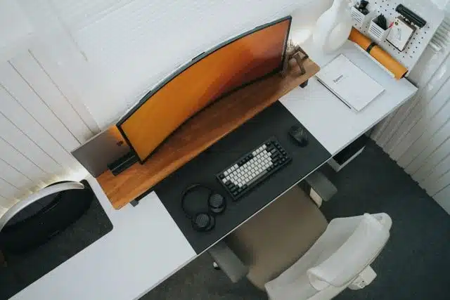 Overhead view of standing desk setup with curved monitor, keyboard, headphones, and desk chair