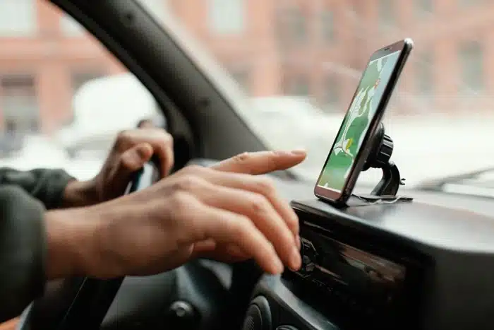 A taxi driver's hands on the steering wheel and dashboard with a navigation app on a mounted phone, representing the taximeter scam that overcharges unsuspecting travelers.
