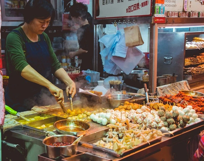 Street food vendor cooking skewers and egg balls at a busy Asian night market stall