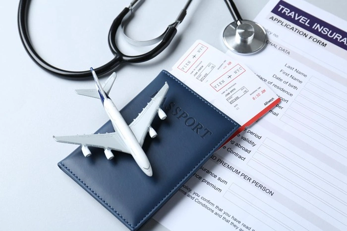 A travel insurance application form alongside a passport, boarding pass, miniature airplane, and stethoscope, representing the process of securing health coverage before traveling overseas