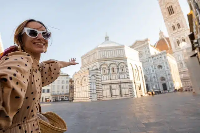 A happy female traveler posing in front of the Florence Cathedral and Baptistery in Piazza del Duomo, Italy