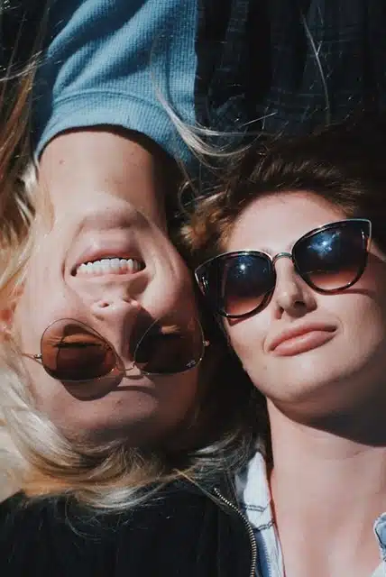 Two women smiling outdoors wearing different sunglasses frame styles