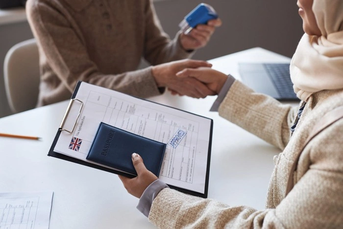 A woman holding a UK passport and visa application form during an appointment, representing the legal insurance requirements tied to certain visa types when traveling abroad