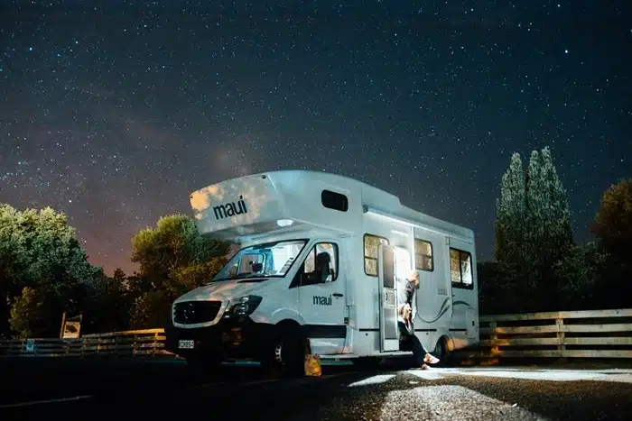 person sitting outside a Maui motorhome parked under a stunning starry night sky surrounded by trees